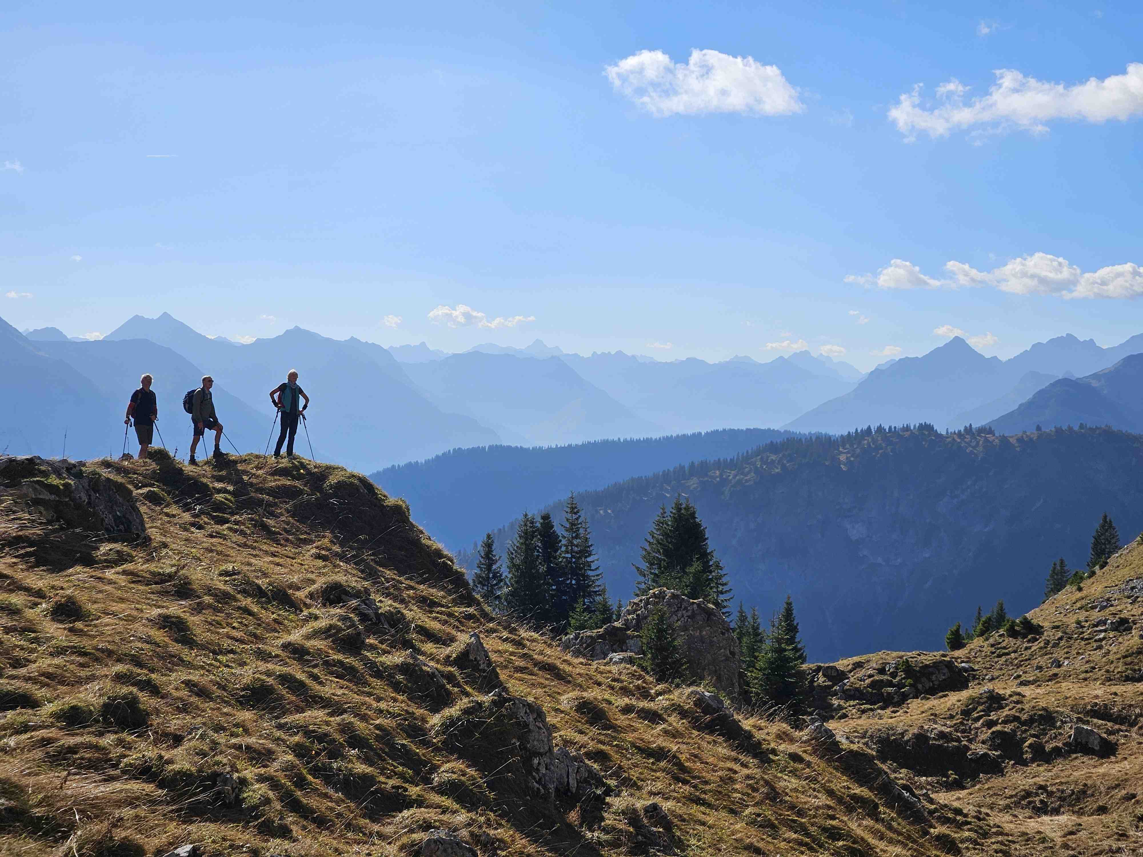 Wanderer stehen auf einer Bergkuppe und schauen in die Ferne
